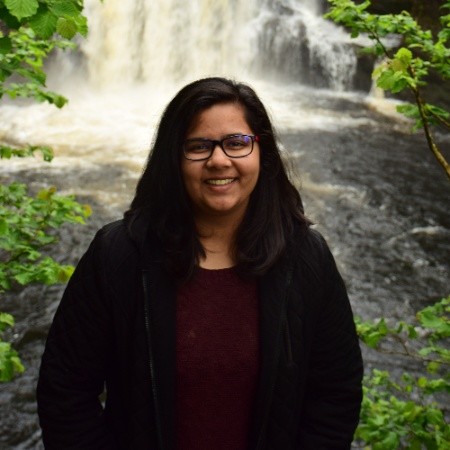 Woman smiling by waterfall, wearing glasses.