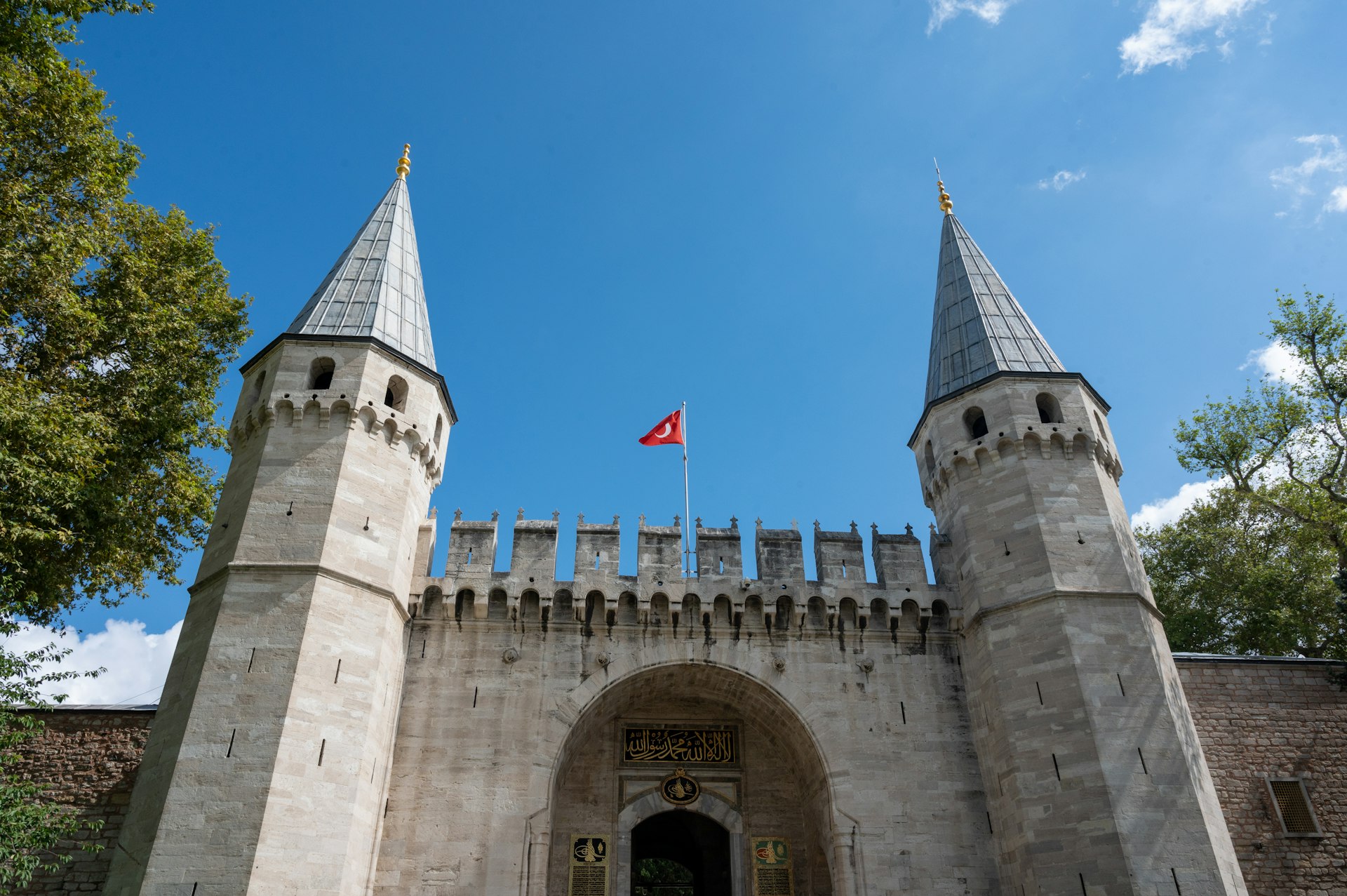 Historic gate with towers and Turkish flag.