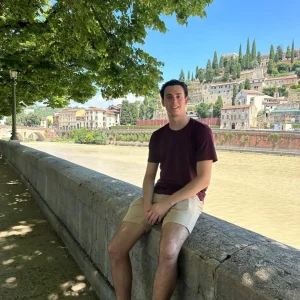 Person sitting on riverside ledge, scenic background.